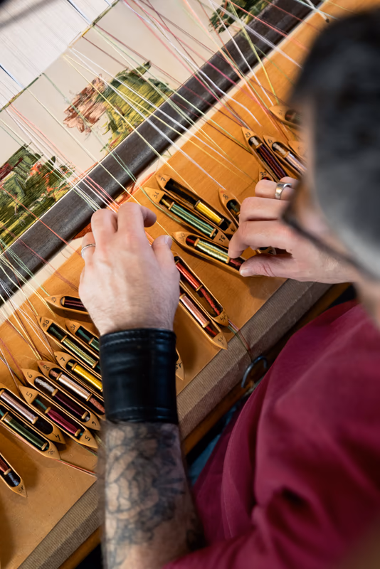 Craftsman's hands handling colorful shuttles on a hand loom
